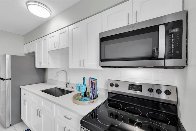 kitchen with appliances with stainless steel finishes, white cabinetry, sink, backsplash, and light tile patterned floors