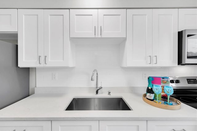 kitchen with decorative backsplash, sink, light stone counters, and white cabinetry