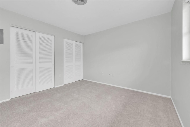 unfurnished bedroom featuring light carpet and two closets