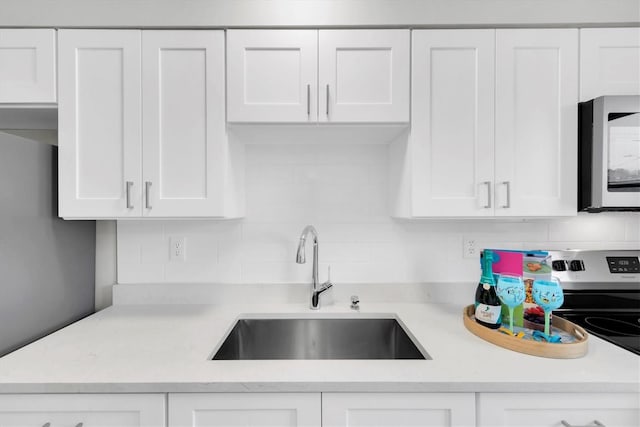 4444 Swift Rd Unit 20, Sarasota, FL 34231 - kitchen featuring stainless steel microwave, a sink, white cabinets, decorative backsplash, and light countertops