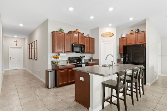 kitchen featuring a breakfast bar, black appliances, sink, light tile patterned floors, and an island with sink