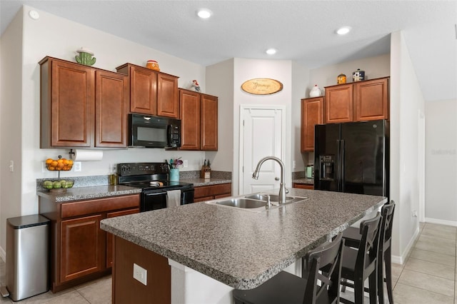 kitchen with a kitchen breakfast bar, a kitchen island with sink, sink, black appliances, and light tile patterned floors