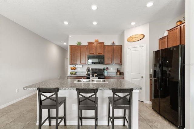 kitchen with sink, black appliances, a center island with sink, a breakfast bar area, and light tile patterned flooring