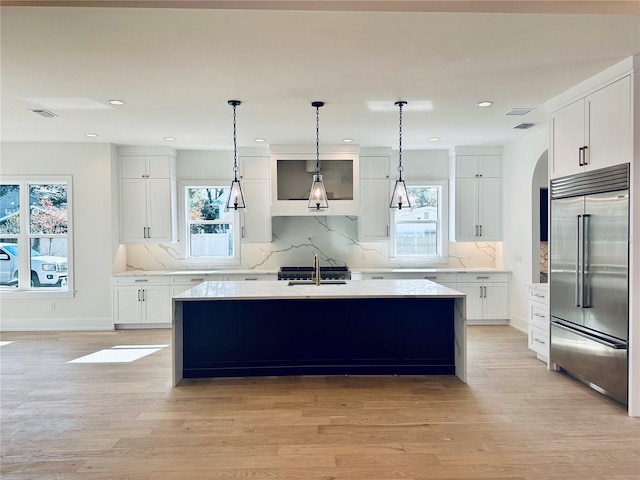 kitchen featuring white cabinetry, a center island with sink, built in fridge, a wealth of natural light, and sink