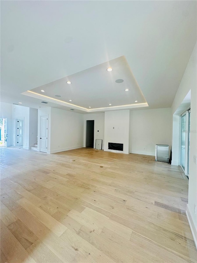 unfurnished living room featuring a raised ceiling and light hardwood / wood-style flooring