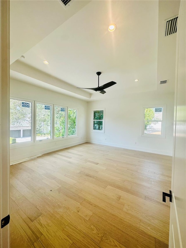 empty room with ceiling fan, a wealth of natural light, and a tray ceiling