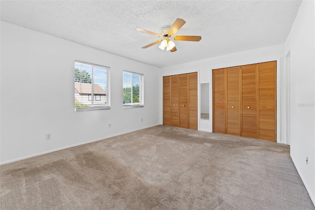 unfurnished bedroom featuring ceiling fan, carpet floors, a textured ceiling, and multiple closets