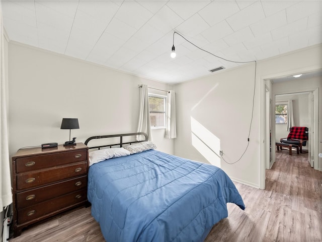 bedroom featuring multiple windows, light hardwood / wood-style floors, and ornamental molding