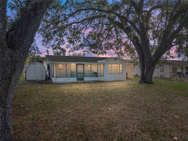 back house at dusk featuring a yard and a storage unit