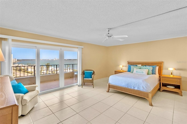 tiled bedroom featuring access to outside, ceiling fan, a water view, and a textured ceiling