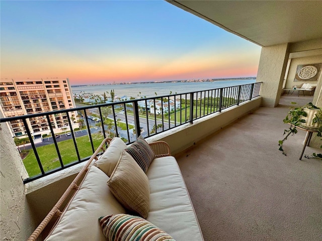 balcony at dusk featuring outdoor lounge area and a water view