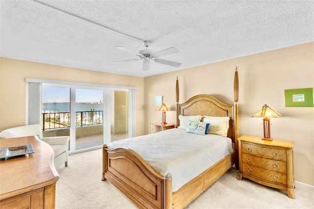 carpeted bedroom featuring access to exterior, ceiling fan, a water view, and a textured ceiling