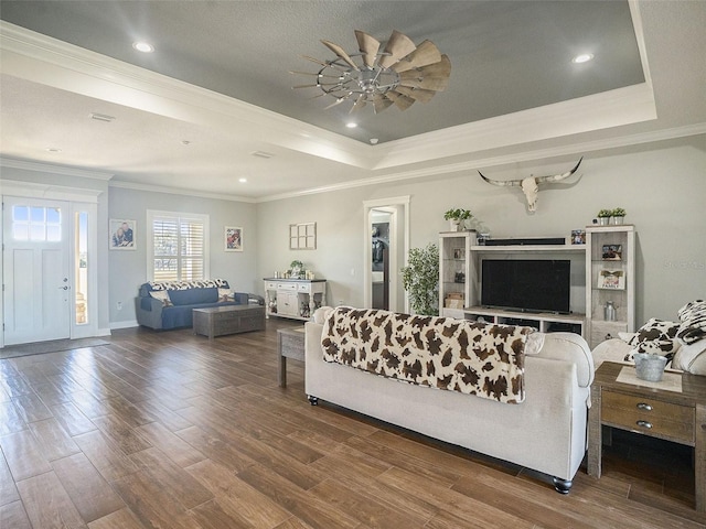 living room with ceiling fan, a raised ceiling, ornamental molding, and dark wood-type flooring