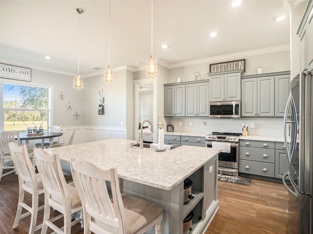 kitchen featuring appliances with stainless steel finishes, dark wood-type flooring, decorative light fixtures, gray cabinets, and an island with sink