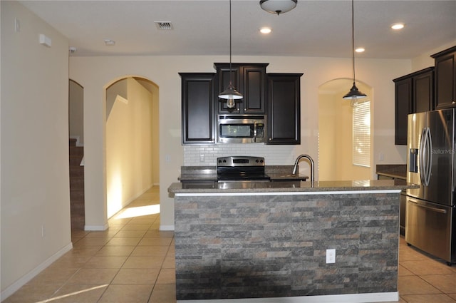 kitchen with a center island with sink, light tile patterned floors, hanging light fixtures, and appliances with stainless steel finishes