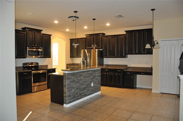 kitchen with a kitchen island with sink, light tile patterned floors, stainless steel appliances, and hanging light fixtures