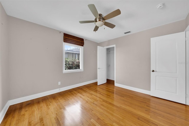 unfurnished bedroom with a walk in closet, ceiling fan, a closet, and hardwood / wood-style flooring