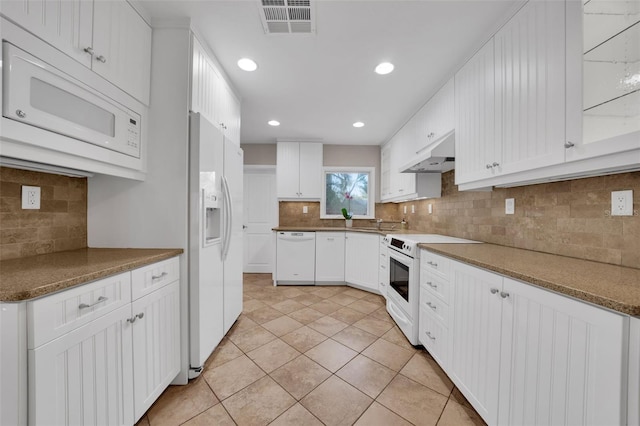 kitchen with white appliances, dark stone counters, decorative backsplash, light tile patterned floors, and white cabinetry