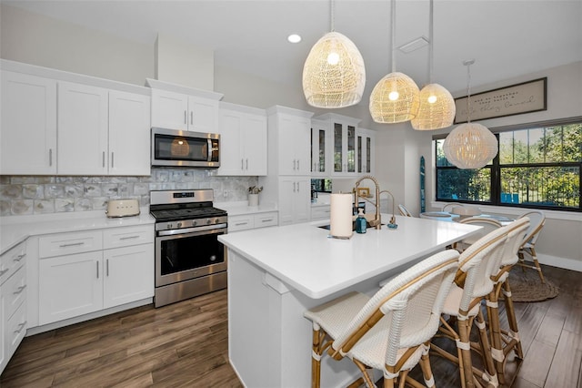 kitchen with stainless steel appliances, white cabinetry, hanging light fixtures, and dark wood-type flooring