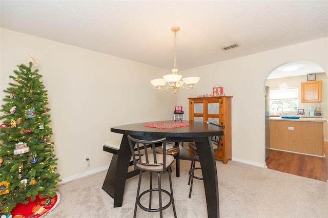 carpeted dining area featuring a notable chandelier, sink, and a textured ceiling