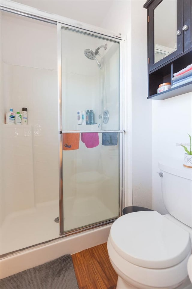 bathroom with hardwood / wood-style flooring, toilet, and a shower with shower door