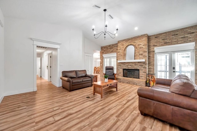 living room with light hardwood / wood-style flooring, high vaulted ceiling, a chandelier, and a brick fireplace