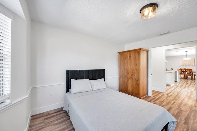 bedroom featuring light hardwood / wood-style flooring, a textured ceiling, and a notable chandelier