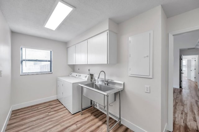 laundry room featuring washer and clothes dryer, cabinets, a textured ceiling, and light hardwood / wood-style flooring