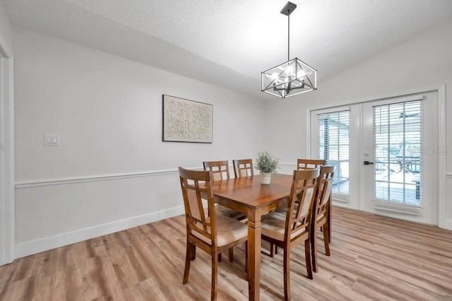 dining space featuring a textured ceiling, light hardwood / wood-style floors, lofted ceiling, and an inviting chandelier