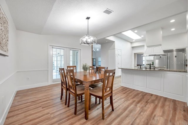 dining area with sink, light hardwood / wood-style flooring, a notable chandelier, a textured ceiling, and vaulted ceiling