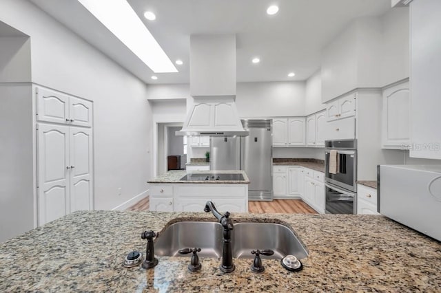 kitchen with light stone countertops, sink, light wood-type flooring, white cabinets, and appliances with stainless steel finishes