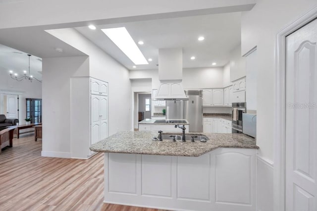 kitchen featuring kitchen peninsula, light hardwood / wood-style floors, white cabinetry, and light stone counters