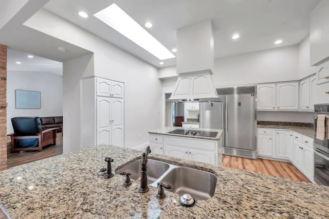 kitchen featuring appliances with stainless steel finishes, light wood-type flooring, a skylight, a center island, and white cabinetry