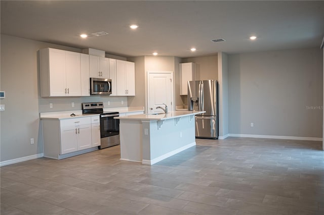 kitchen with a breakfast bar, stainless steel appliances, sink, white cabinetry, and an island with sink