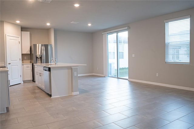 kitchen with stainless steel appliances, a center island with sink, white cabinetry, and a wealth of natural light