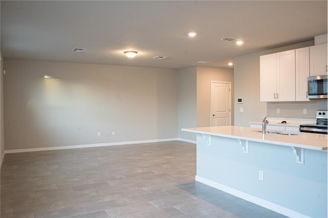 kitchen featuring sink, stainless steel appliances, a kitchen breakfast bar, a center island with sink, and white cabinets