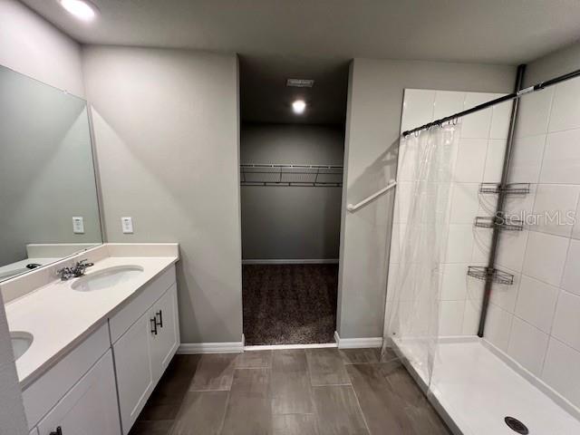 full bathroom featuring a tile shower, a spacious closet, double vanity, a sink, and baseboards