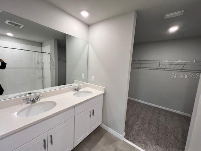 bathroom featuring baseboards, visible vents, a sink, and a walk in closet