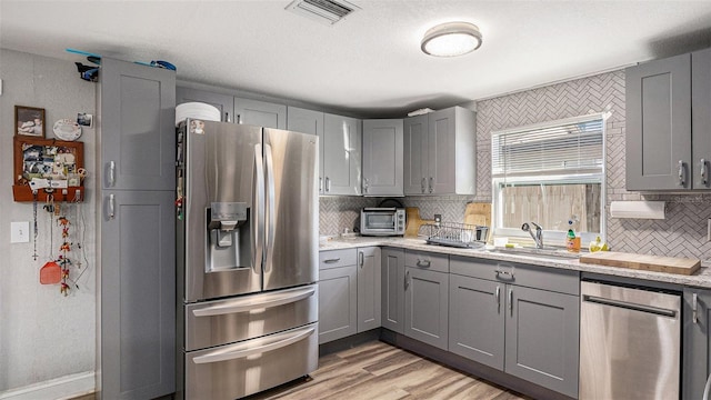 kitchen featuring sink, gray cabinetry, light stone counters, light hardwood / wood-style floors, and stainless steel appliances