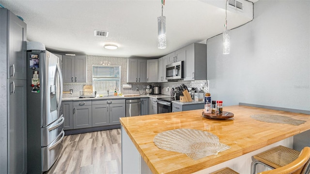 kitchen featuring appliances with stainless steel finishes, gray cabinetry, decorative backsplash, sink, and decorative light fixtures