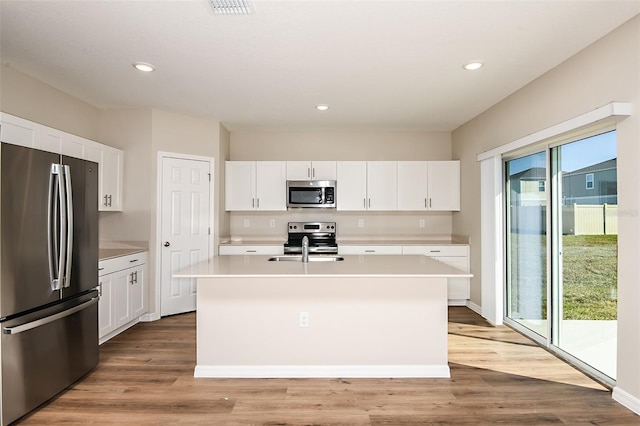 kitchen with appliances with stainless steel finishes, sink, a center island with sink, light hardwood / wood-style floors, and white cabinetry