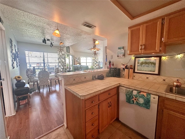 kitchen with dishwasher, a textured ceiling, a peninsula, and tile counters