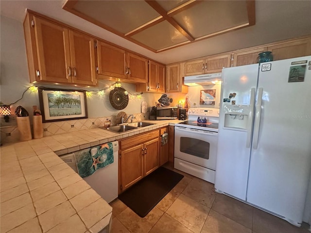 kitchen featuring tile patterned floors, under cabinet range hood, a sink, tile countertops, and white appliances