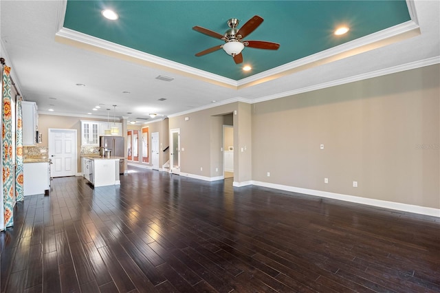 unfurnished living room featuring a tray ceiling, crown molding, ceiling fan, and dark wood-type flooring