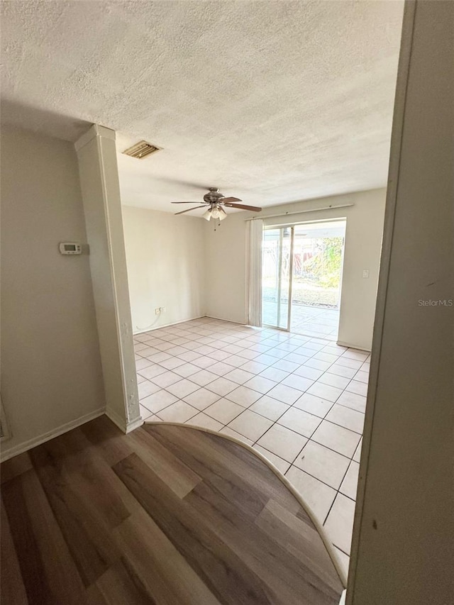 empty room featuring ceiling fan, light tile patterned flooring, and a textured ceiling