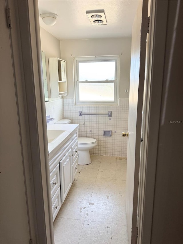 bathroom featuring vanity, toilet, and tile walls