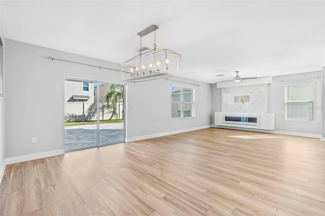 unfurnished living room with ceiling fan with notable chandelier and light wood-type flooring