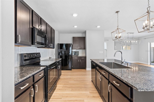 kitchen with a kitchen island with sink, black appliances, sink, light wood-type flooring, and decorative light fixtures