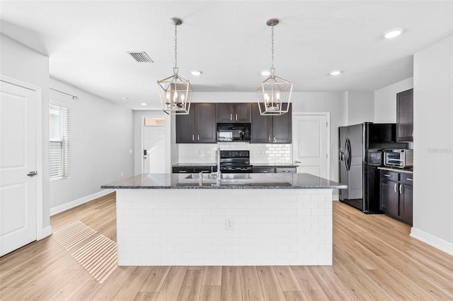 kitchen with dark brown cabinets, light hardwood / wood-style flooring, black appliances, and a center island with sink