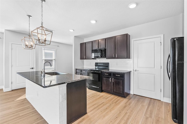 kitchen with pendant lighting, black appliances, sink, an island with sink, and light hardwood / wood-style floors